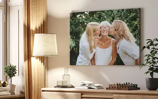 A canvas print hanging above a desk of two blonde women kissing a happy lady on the cheek.