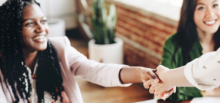 Two people shaking hands, we only can see the face of one of them who is smiling.