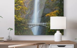 A metal canvas print of a landscape hanging above a desk.