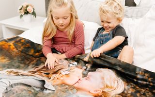 Children snuggled in bed, wrapped in their personalized photo blanket.