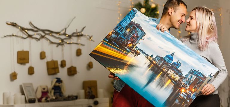 A happy couple looking at each other holding a landscape canvas print.