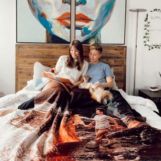 Couple on a bed with their dogs, wrapped in a custom fleece photo blanket, reading together.