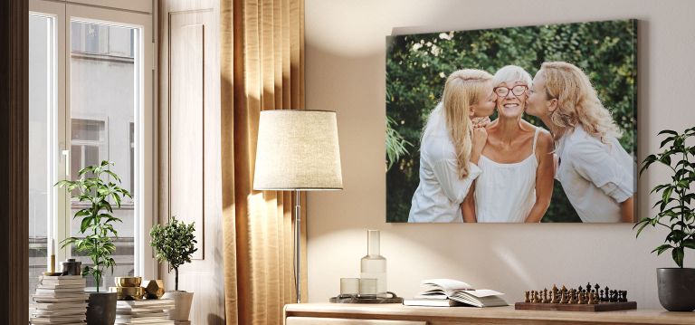 A canvas print hanging above a desk of two blonde women kissing a happy lady on the cheek.