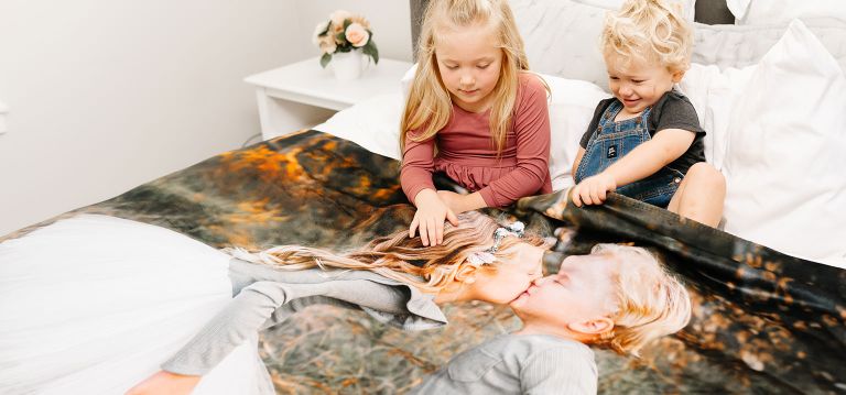 Children snuggled in bed, wrapped in their personalized photo blanket.