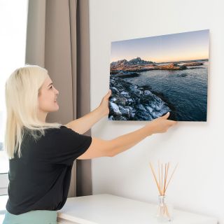 A woman hanging a landscape canvas print on the wall.