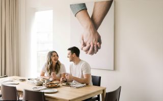 A couple sitting at a table with a canvas print of them holding hands on the wall behind them.