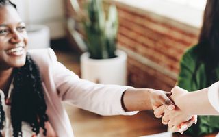 Two people shaking hands, we only can see the face of one of them who is smiling.