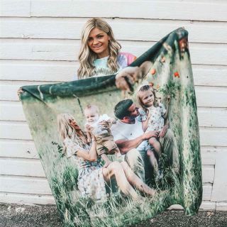 Woman smiling while holding up her own personalized photo blanket of her family.