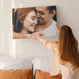 A woman hanging a canvas print with a photo of a happy couple on the wall.