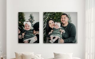 Christmas themed canvas prints of a family with baby hanging on a wall above a modern couch with bright white Christmas tree accents in the background