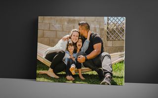 Canvas print featuring a joyful family of four sitting on a hammock outdoors, with the father kissing the mother on the forehead while their children smile and embrace each other.